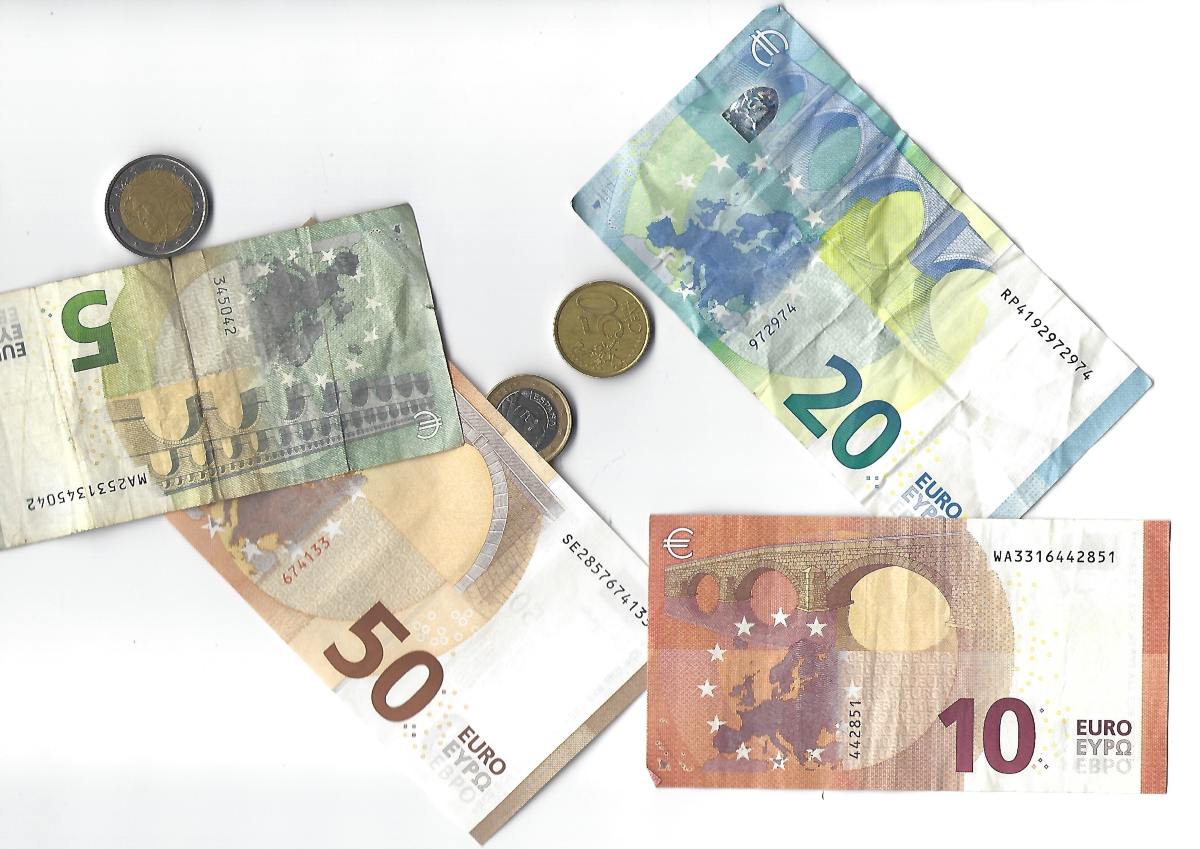 Composizione di banconote da 5, 10, 20 e 50 euro stropicciate e monete sparse su sfondo bianco.
